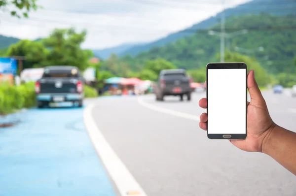 La mano del hombre sostiene el teléfono móvil sobre el coche borroso en la carretera — Foto de Stock