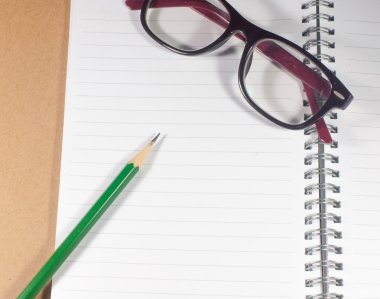 Açık boş defter ile yeşil kalem, gözlük ve çizgili sayfa