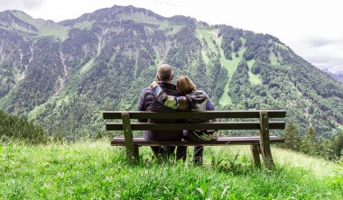 Couple sitting on a bench looking at the alpine landscape in the Allgau. Bavaria. clipart