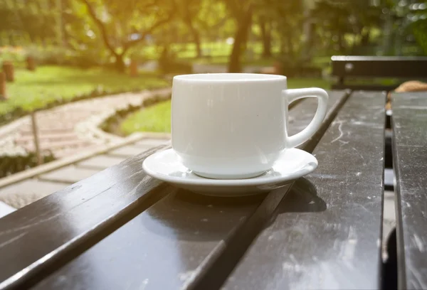 Чашка кави на столі в саду в сонячний день, розмита — стокове фото