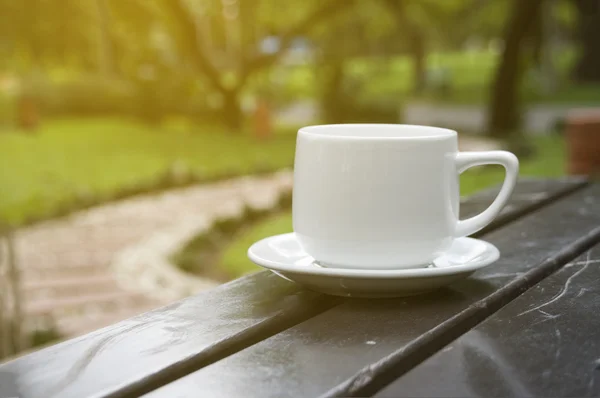 Чашка кави на столі в саду в сонячний день, розмита — стокове фото