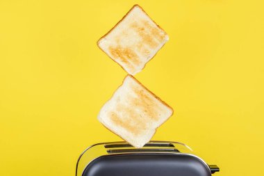 Ekmek kızartma makinesinden fırlayan tost dilimleri sarı arka planda.