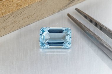 macro mineral faceted stone aquamarine with tweezers on a gray background close-up clipart