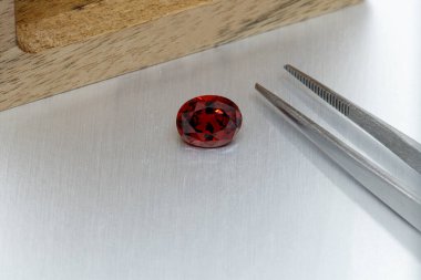 macro mineral faceted stone Garnet with tweezers on a gray background close-up clipart