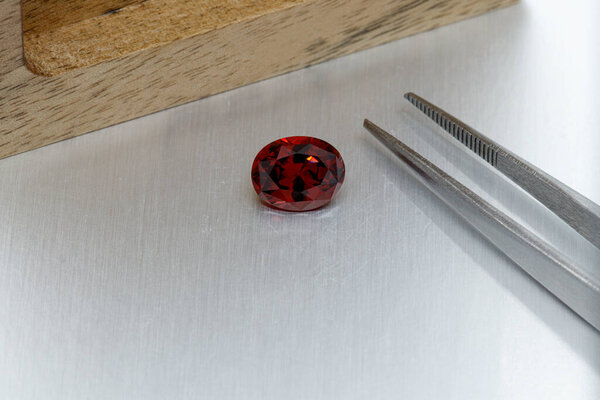 macro mineral faceted stone Garnet with tweezers on a gray background close-up