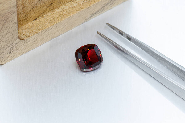 macro mineral faceted stone Garnet with tweezers on a gray background close-up