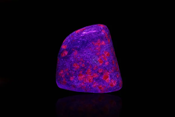 macro mineral stone ruby under ultraviolet light on a black background close-up