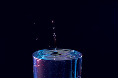 Su damlası düşüyor, makro sıçrama. Doğal ve karanlık bir arkaplanda yakın plan.