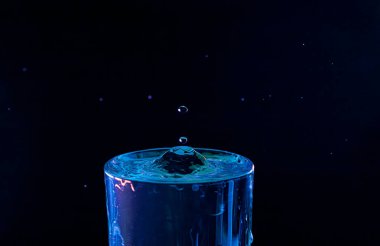 Su damlası düşüyor, makro sıçrama. Doğal ve karanlık bir arkaplanda yakın plan.