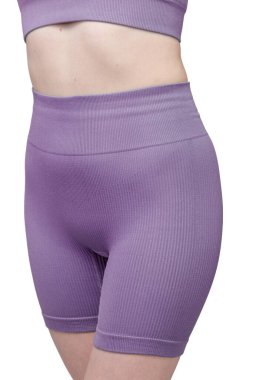 Formda bir kadının sırtından atölye çekiminde, gri çatallı, pürüzsüz spor şortu ve uyumlu spor sutyeni sergileniyor. Kumaş desenli bir örgü. Beyaz arka planda izole edilmiş. Spor giyim, spor giyim ve fitness programları için ideal.