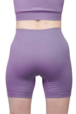 Formda bir kadının sırtından atölye çekiminde, gri çatallı, pürüzsüz spor şortu ve uyumlu spor sutyeni sergileniyor. Kumaş desenli bir örgü. Beyaz arka planda izole edilmiş. Spor giyim, spor giyim ve fitness programları için ideal.