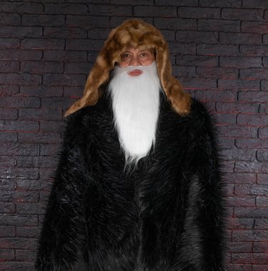 Siyah arka planda siyah kürklü beyaz sakallı Noel Baba portresi.