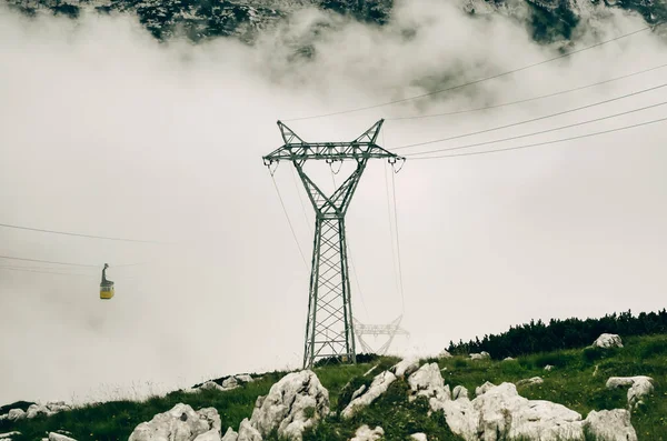Alp Dağları 'nın tepesindeki bulutların arasından geçen bir teleferik. Yalnız sarı bir taksi gökyüzünde süzülüyor..