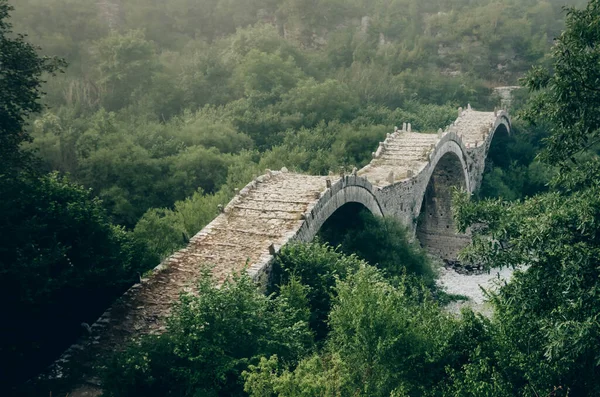 Sis ve Plakidas 'ın antik taş köprüsü şafak vakti kurak bir nehrin yatağının üzerinde. Zagori bölgesi, Yunanistan Vikos Vadisi Ulusal Parkı.