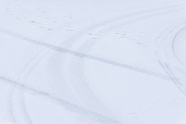 Karla kaplı bir yolda araç izleri var.