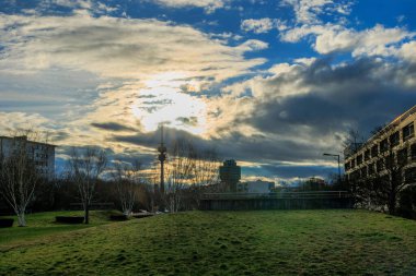 Gün batımında güneş ve bulutların dramatik bir karışımı televizyon kulesi ve Milbertshofen Almanya Münih 'teki Petuelpark' taki BMW şirket binası manzarası 16.3.2024