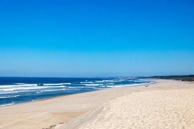 Açık mavi gökyüzü altında dalgalanan geniş kumlu Atlantik plajı Portekiz, Ovar Furadouro, 10 Ekim 2025.