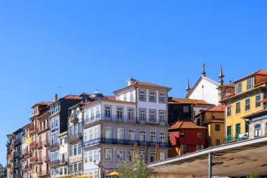 Ribeira ilçesi, Portekiz, Porto, 11 Ekim 2025 üzerinde yükselen kilise kuleleri olan parlak renkli nehir kenarlı binalar.