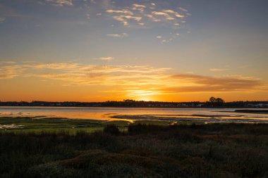 Katmanlı günbatımı bulutları Furadouro Portekiz 'deki sakin lagün manzarası üzerinde parlıyor, Ovar Furadouro, 12 Kasım 2025.