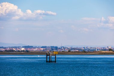 Uzak şehir silueti ve yumuşak bulutlarla durgun nehir suyunda duran seyrüsefer platformu, Portekiz, Aveiro, 13 Ekim 2025
