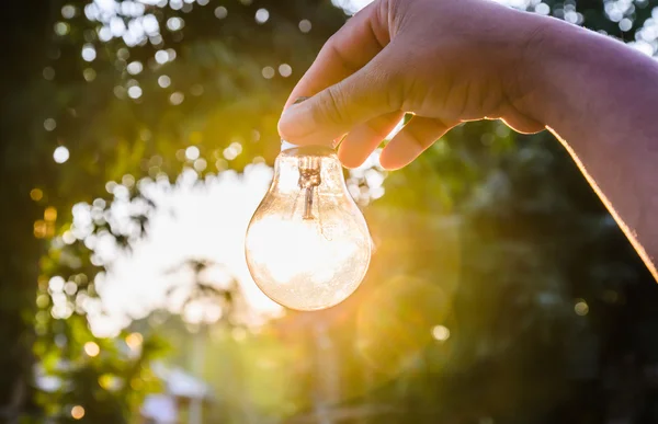 Mão segurando uma lâmpada com o conceito de energia por do sol — Fotografia de Stock