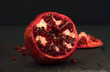 Siyah arka planda açık nar. Olgun meyveler ve serpilmiş taneler.