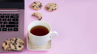 Bir fincan çay, dizüstü bilgisayarın yanındaki bir fincan tabakta. Çikolatalı kurabiye.