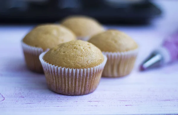 Čerstvě upečené muffiny připravené k ozdobení, s taškou na pečivo naplněnou smetanou — Stock fotografie