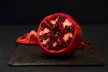 Siyah arka planda serpiştirilmiş tohumlarla açık nar. Büyük kırmızı meyve