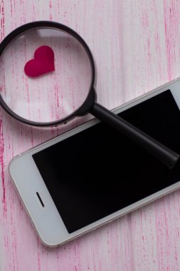 Kalp büyüteç altında, beyaz bir cep telefonunun yanında yatıyor.. 