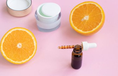 Pipette yüz serumu, krema ve turunçgiller pembe arka planda.. 