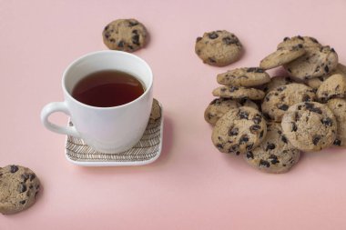 Pembe arka planda bir fincan çay ve bir sürü kurabiye. Aşırı yeme kavramı