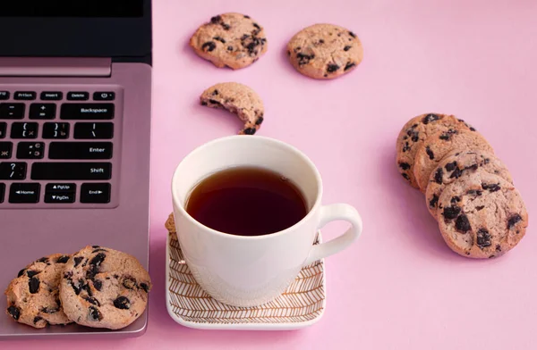 a cup of tea is on a saucer near a laptop. Cookies with chocolate