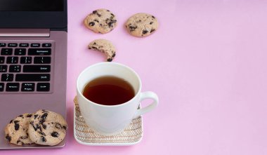 Ev bilgisayarı, çikolatalı kurabiye ve çay fincanı.