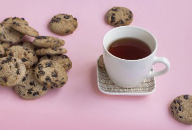 Pembe arka planda bir fincan çay ve bir sürü kurabiye. Aşırı yeme kavramı