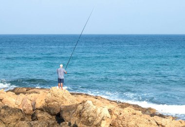 Tanınmayan bir erkek balıkçı sahilde durur ve oltayı atar.