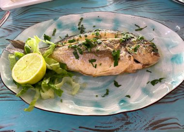 Limon ve otlarla dolu bir tabakta kızarmış levrek balığı servis ediyorum.. 