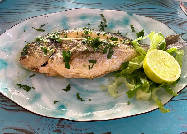 Servir pescado frito de lubina en un plato con limón y hierbas. —  Fotos de Stock