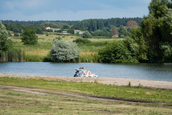 Two girls are lying on sun loungers by a small lake. Pond in the village. — Stock Photo, Image