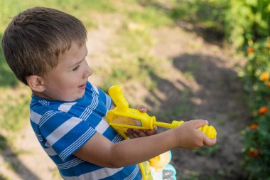Su tabancalı, komik suratlar yapan, yaz parkında su sıçratan neşeli çocukluk anları, aktif açık hava eğlencesi ve mutlu çocuk yaşam tarzı olan beş yaşında bir çocuk. Yüksek kalite fotoğraf