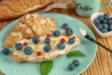 Krem peynirli taze kruvasan, mavi tabakta yabanmersini ve bal, tatlı kahvaltı veya yakın plan tatlı. Sağlıklı, kaliteli, kafe konsepti. Kruvasan dolgu fikirleri. Yüksek kalite fotoğraf