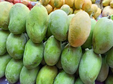 Açık hava meyve tezgahında yığınla yeşil mango meyvesi.