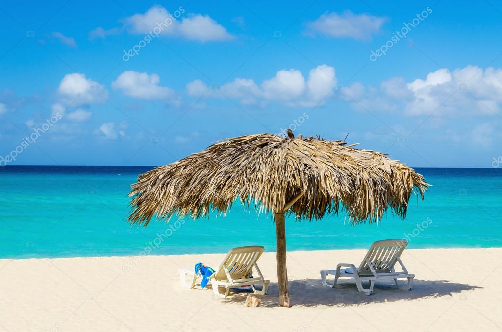 Amazing tropical beach with sunbeds and palm tree umbrellas, golden sand, azure water and blue sky, Caribbean Islands