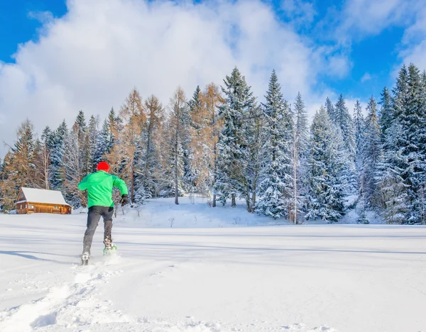 Hombre con chaqueta verde y gorra roja corre en la nieve — Foto de Stock