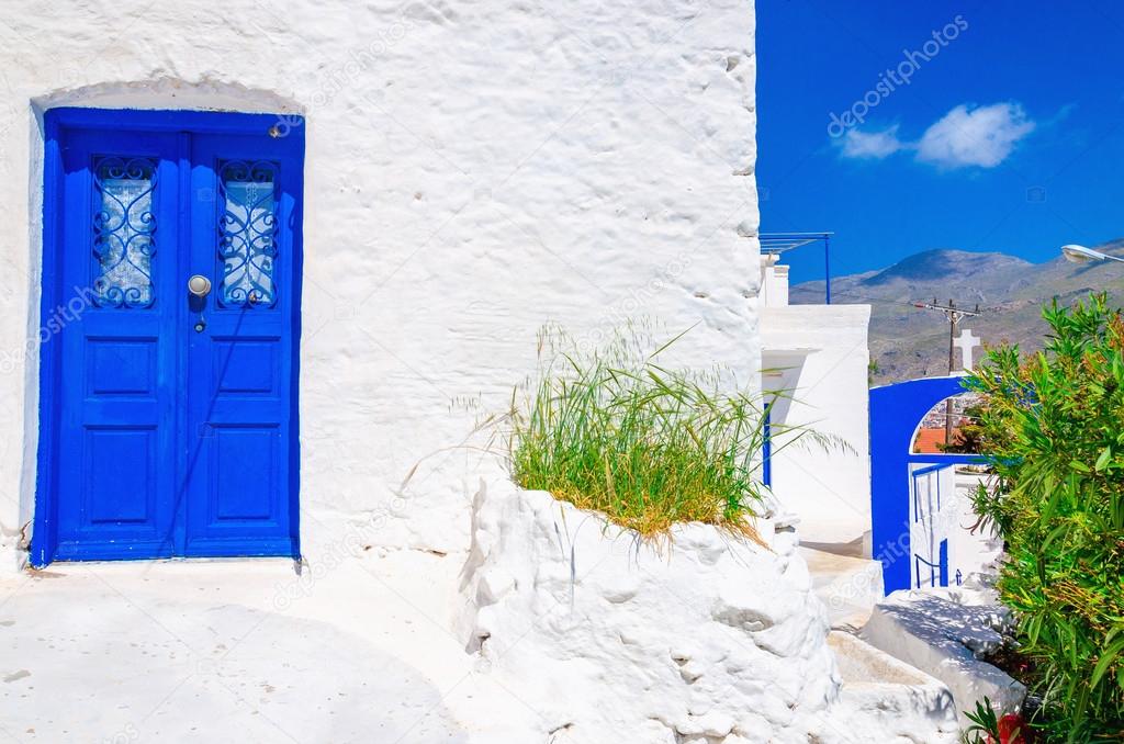 Blue wooden door, white wall and flowers in Greece