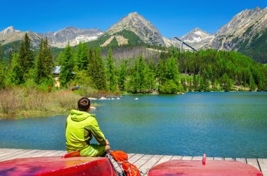Young man at pier mountain lake with high peaks