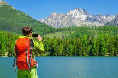 man takes a photo of mountain lake