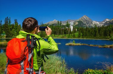 man takes picture of mountains and lake
