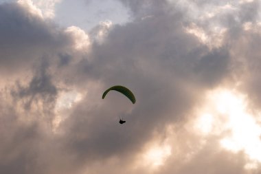 Gün batımında ya da gün doğumunda bulutların üzerinde uçan bir paraglider silueti.
