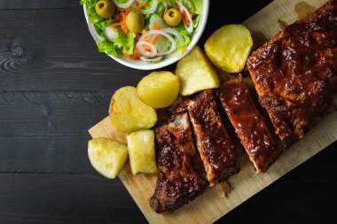 Barbekü pirzola, patates ve salata. Koyu bir arka planda tahta bir tahta üzerinde. Boşluğu kopyala.